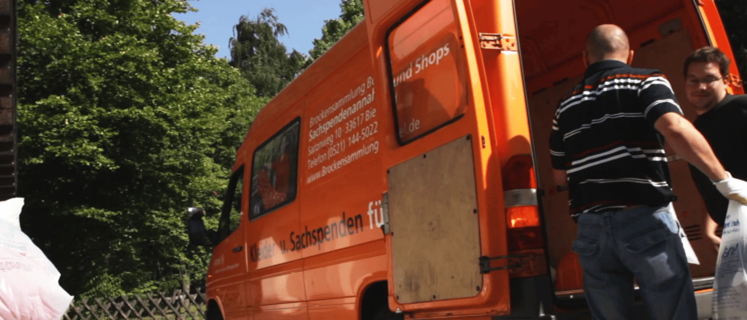 Das Bild zeigt zwei Personen, die Kleidersäcke in ein Fahrzeug der Bethel-Stfitung 