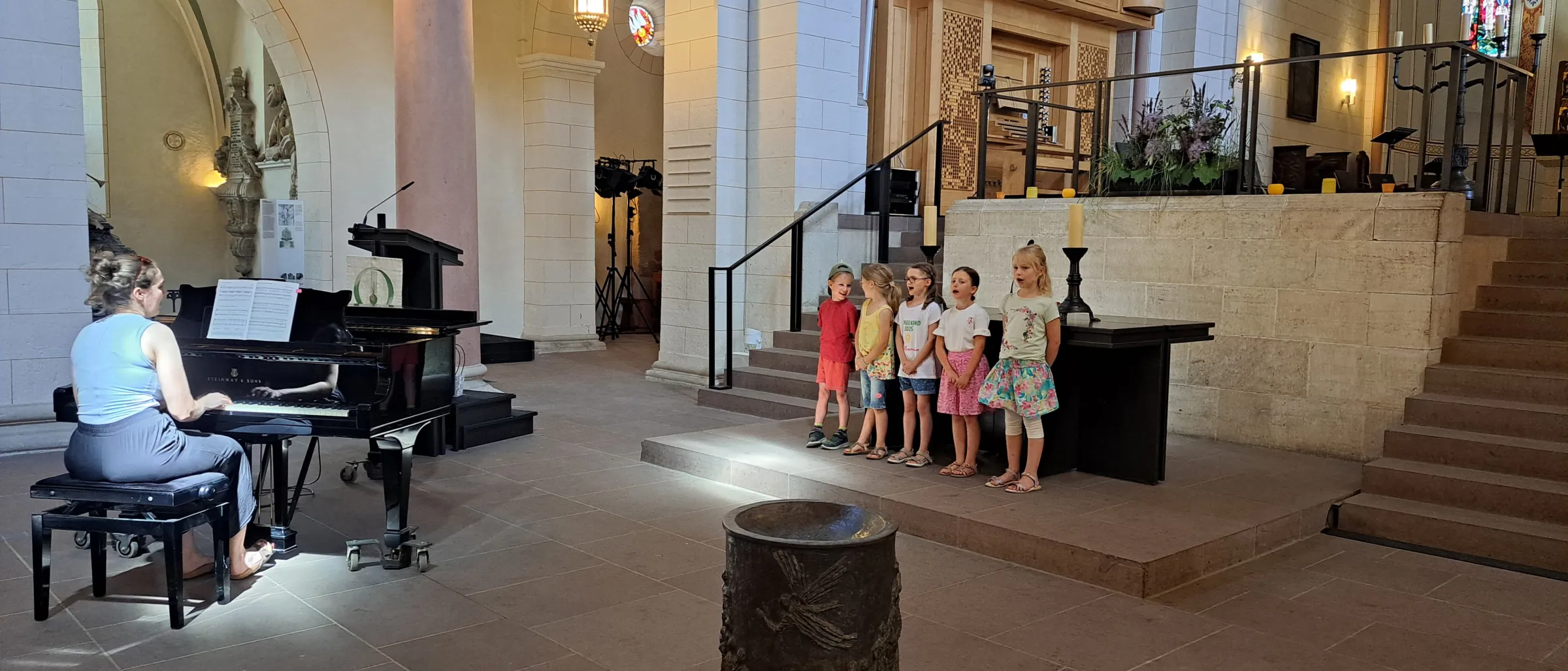 Zu sehen sind die Kinder der Chorgruppe 1 vor dem Altar der Stiftskirche. Am Flügel sitzt Kantorin Lisbeth Amnberger