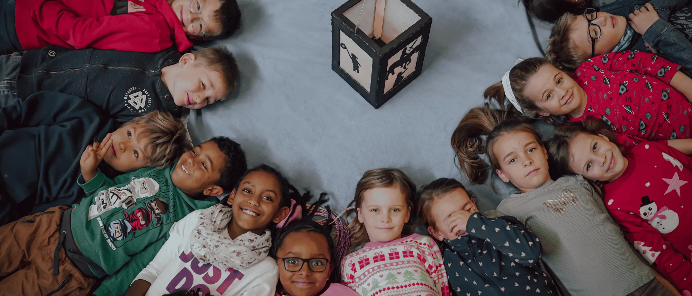 Die Kinder der Kinderkirche liegen auf einem Foto im Kreis, in der Mitte eind Windlicht mit einer Kerze