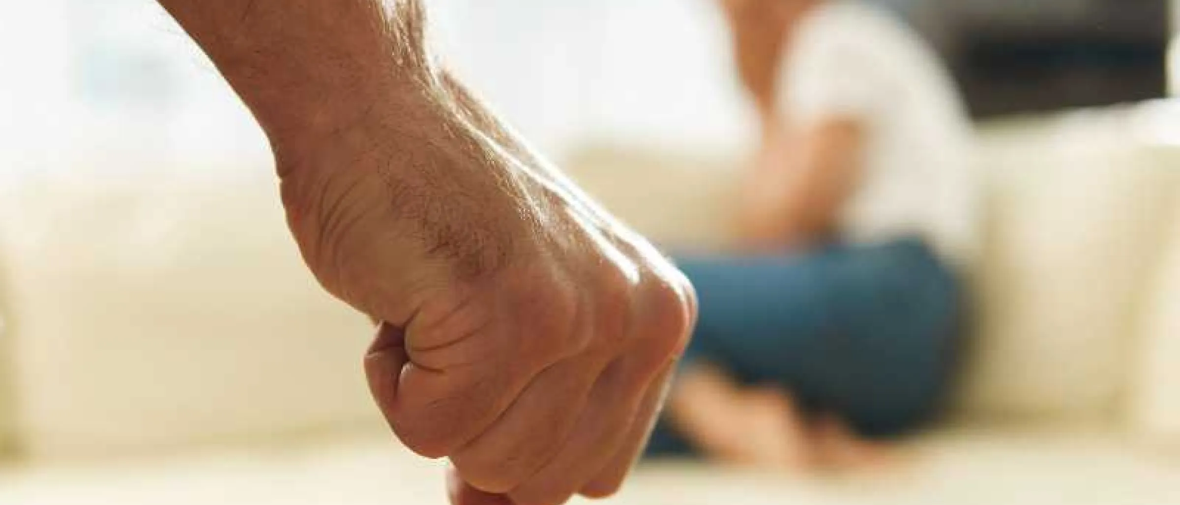 Das Symbolbild zeigt eine Faust. Im Hintergrund ist verschwommen eine weibliche Person zu sehen.