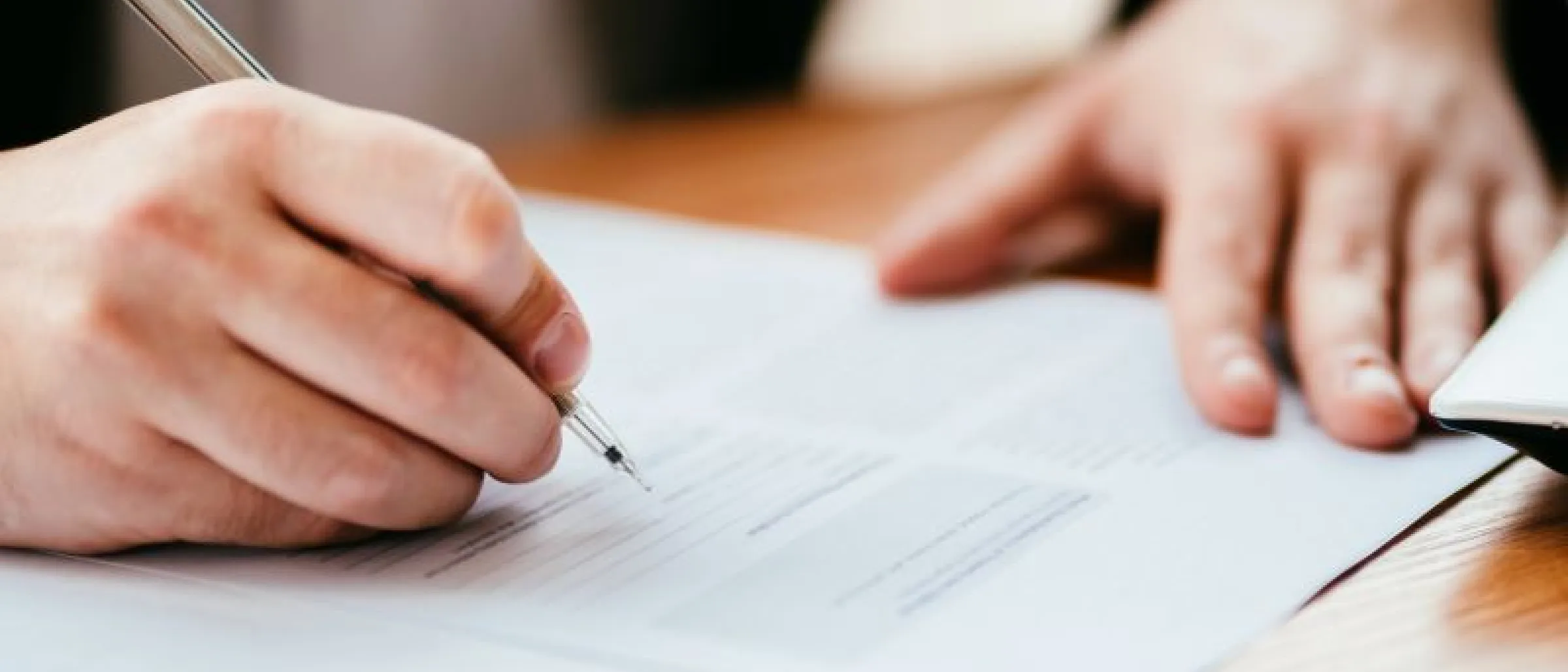 Das Bild zeigt symbolisch eine Hand, die einen Kugelschreiber hält und ein Formular ausfüllt