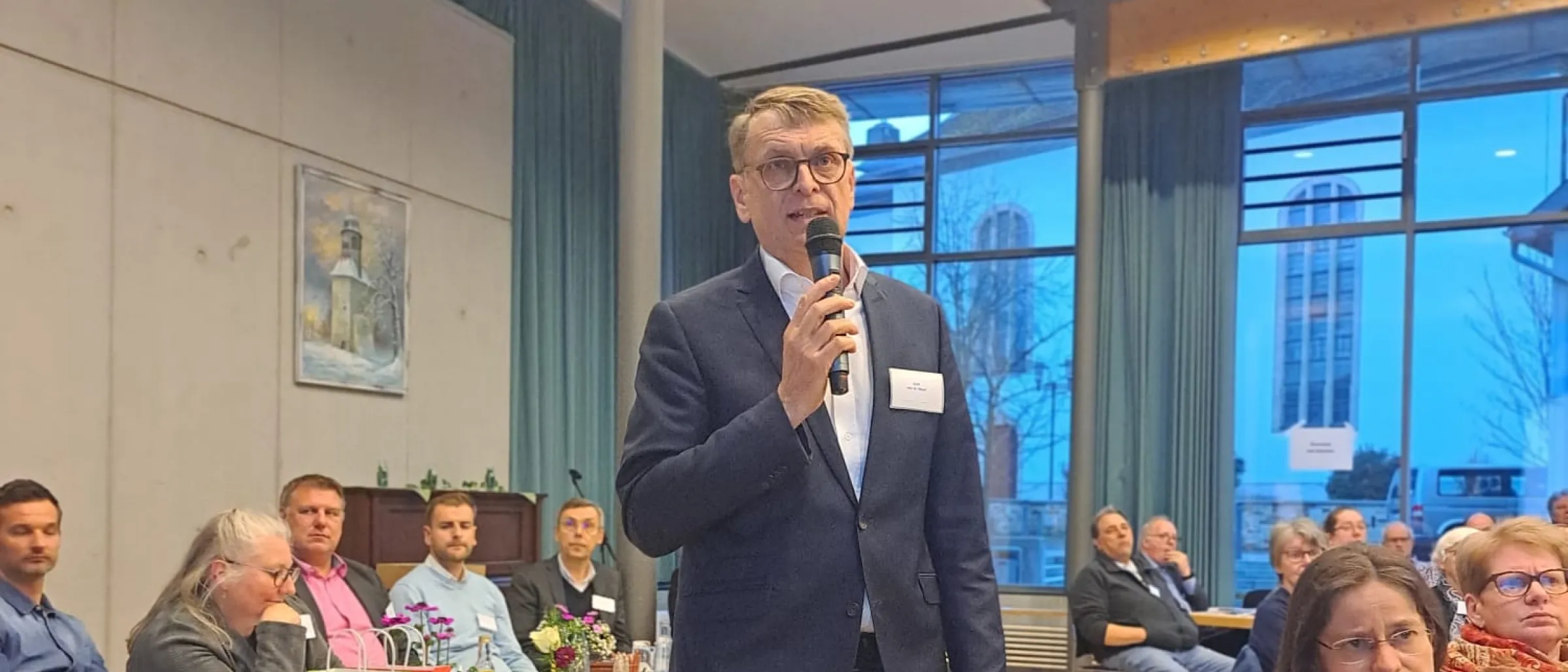 Dr. Jörg Mayer, Leiter der Finanzabteilung und Mitglied der Kirchenregierung, spricht mit Mikro vor den Teilnehmer*innen