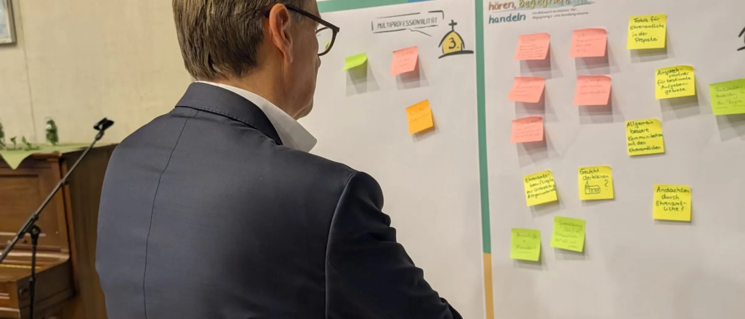 Dr. Jörg Mayer steht vor einer Stellwand mit Post-Its. Er sieht sich die Ergebnisse der sogenannten Murmelgruppen nach dem ersten Teil der Präsentation an. Es ging um erste Einschätzungen zu den genannten Säulen, die sich wesentlich verändern werden. 