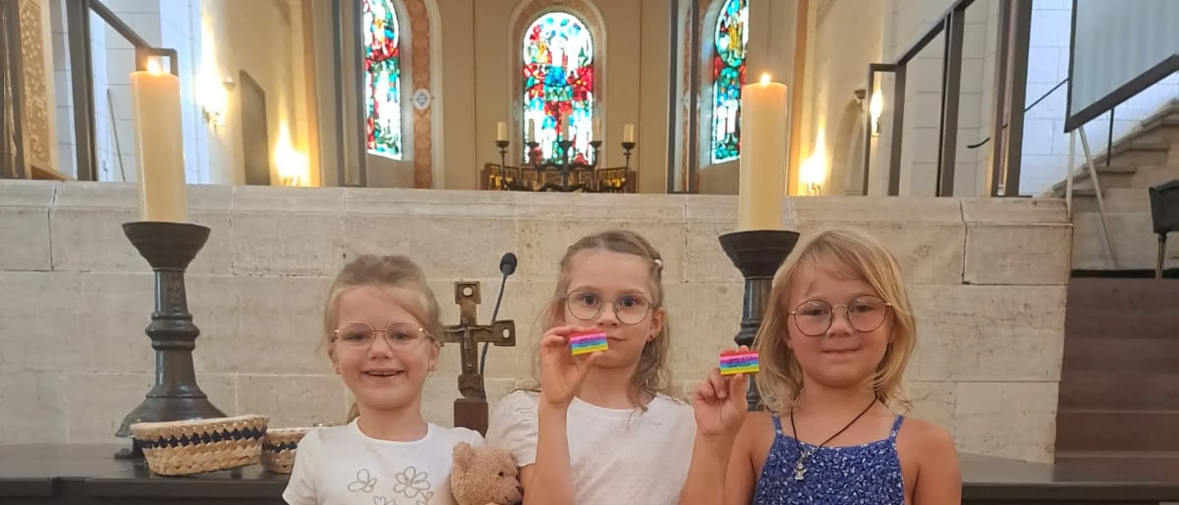 Die Erstklässlerinnen Charlotte Feg, Katharina Mamel und Nele Schick stehen vor dem Altar und zeigen stolz ihre Geschenke
