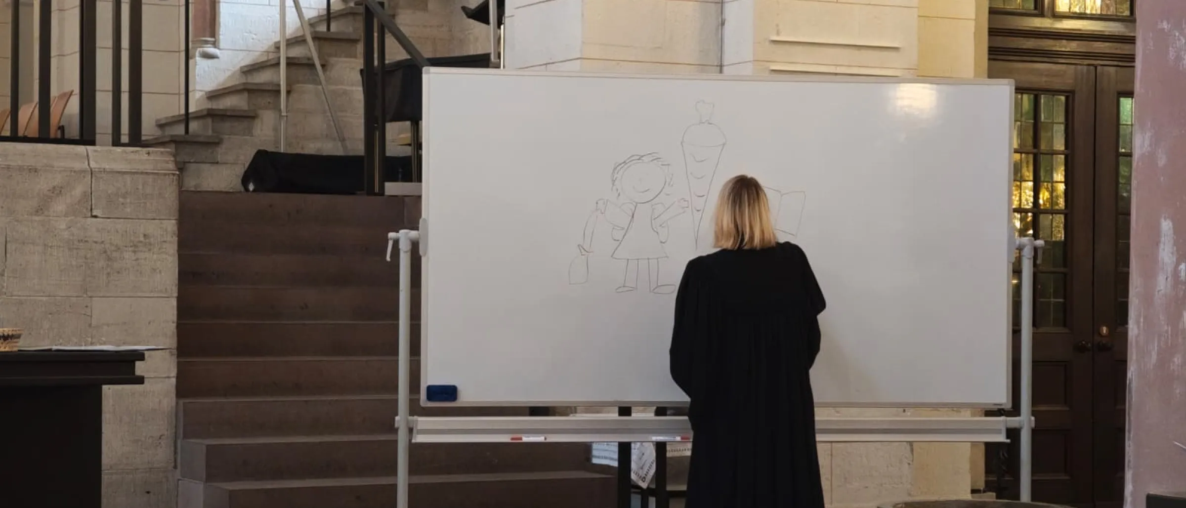 Pröpstin Meike Bräuer-Ehgart steht an einer Tafel und malt auf, was Kinder in der Schule brauchen